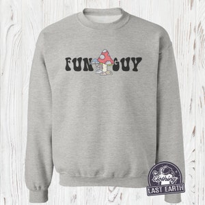 K&ouml;nnte beinhalten: Ein graues Sweatshirt mit dem Text "FUN GUY" in schwarzen Buchstaben. Der Text ist mittig auf dem Sweatshirt platziert und wird von einem Cartoon-Bild von drei Pilzen begleitet, einem roten mit wei&szlig;en Punkten, einem blauen und einem braunen.