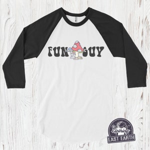 K&ouml;nnte beinhalten: Ein wei&szlig;es und schwarzes Baseball-T-Shirt mit einem bunten Pilz-Motiv und dem Text "FUN GUY" in einer Retro-Schrift.