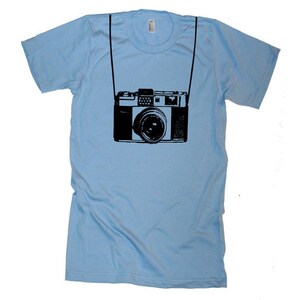 May include: A light blue t-shirt with a black silhouette of a vintage camera.