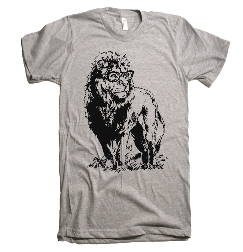 May include: A gray t-shirt with a black and white illustration of a lion wearing glasses. The lion is standing in a grassy field.