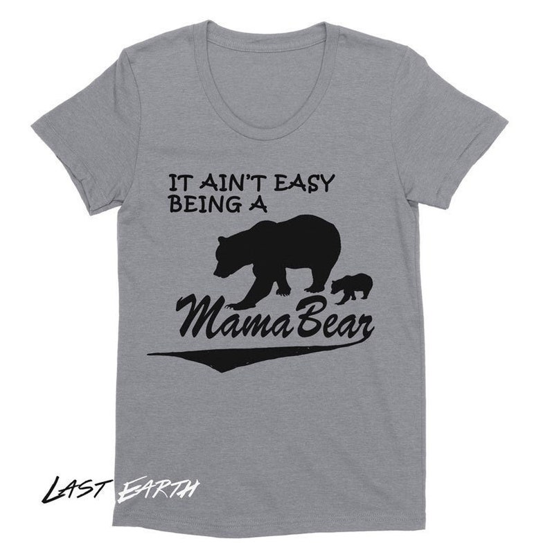 May include: A heather gray t-shirt with a crew neck. The shirt features the text "IT AIN'T EASY BEING A Mama Bear" in black, along with a silhouette of a bear and a cub. The brand name "LAST EARTH" is printed at the bottom.