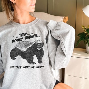 May include: A gray sweatshirt with a black and white illustration of a honey badger. The text "Team Honey Badger" and "We take what we want!" is printed on the sweatshirt.