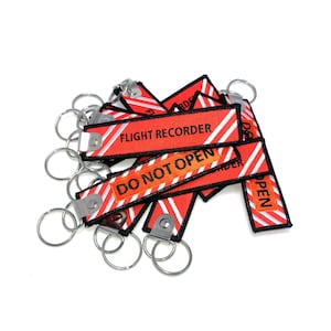 May include: A collection of red and white striped keychains with the text "FLIGHT RECORDER" and "DO NOT OPEN". The keychains have silver key rings attached. The keychains are a bright red color with white diagonal stripes.