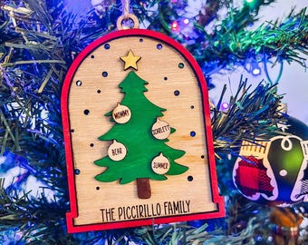 May include: A wooden Christmas tree decoration with a red border and a natural wood interior. The decoration features a green Christmas tree with names on the ornaments and the text "THE PICCIRILLO FAMILY". A gold star sits atop the tree.