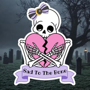 May include: A white cartoon skull with a purple bow and a broken pink heart held by skeletal hands. The text "Sad To The Bone" is on a purple banner. The background shows a graveyard with a spooky tree.