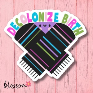 May include: A sticker with the text "DECOLONIZE BIRTH" in pink, green, and blue. The sticker features a black design with colorful stripes and a smiling face. The background is a pink wooden surface.