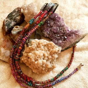 Peut inclure: Trois mèches de rallonges de cheveux tressées colorées avec des clips en métal argenté en haut. Les extensions sont faites de tissu tissé et ont de petites perles argentées tout au long. Les extensions sont présentées sur une surface blanche avec des cristaux d'améthyste.