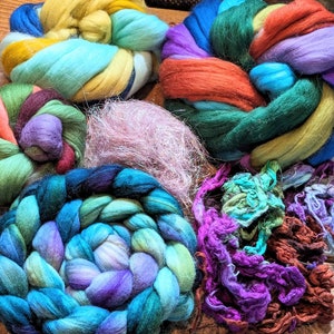 May include: A collection of colorful yarn in various textures and colors, including teal, purple, pink, green, and orange. The yarn is arranged in a pile on a wooden surface.