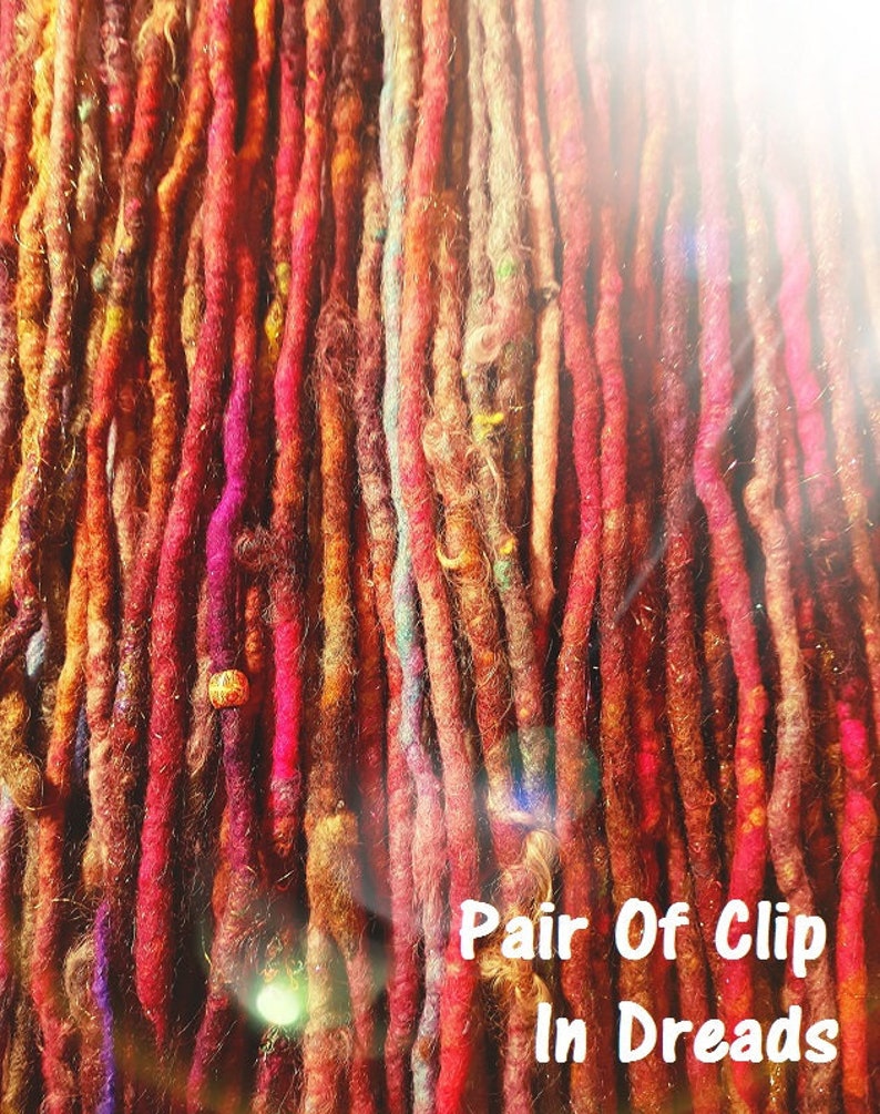 May include: A close-up of a bundle of colorful wool dreadlocks with beads. The dreadlocks are in various shades of red, orange, and brown. The text "Pair Of Clip In Dreads" is visible at the bottom of the image.