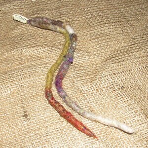 May include: Two long strands of synthetic hair, one brown, one white, with a purple and green ombre effect. The strands are tied together with a small plastic hair clip.