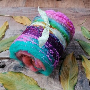 May include: A colorful roll of yarn with a light green ribbon tied around it. The yarn is a mix of pink, purple, blue, green, and yellow.