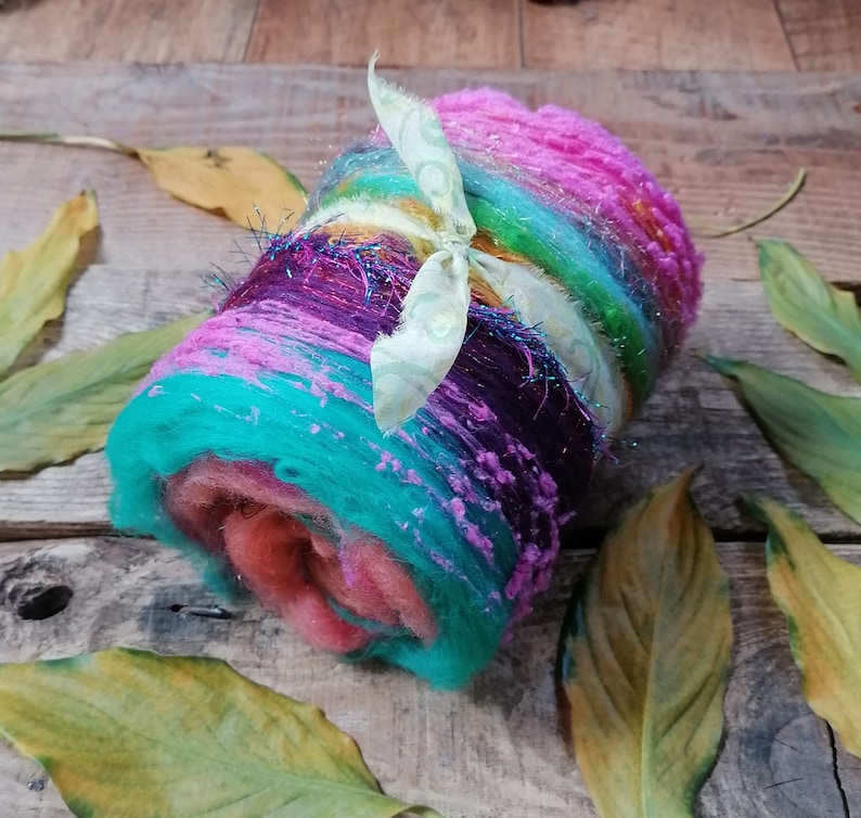 May include: A colorful roll of yarn with a light green ribbon tied around it. The yarn is a mix of pink, purple, blue, green, and yellow.