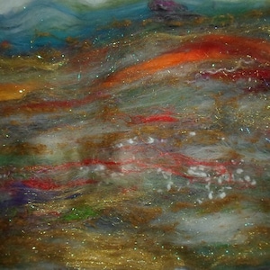 May include: Abstract art piece made with wool fibers in shades of blue, green, orange, red, and white. The fibers are layered and textured, creating a sense of depth and movement. The piece is accented with gold glitter, adding a touch of sparkle.