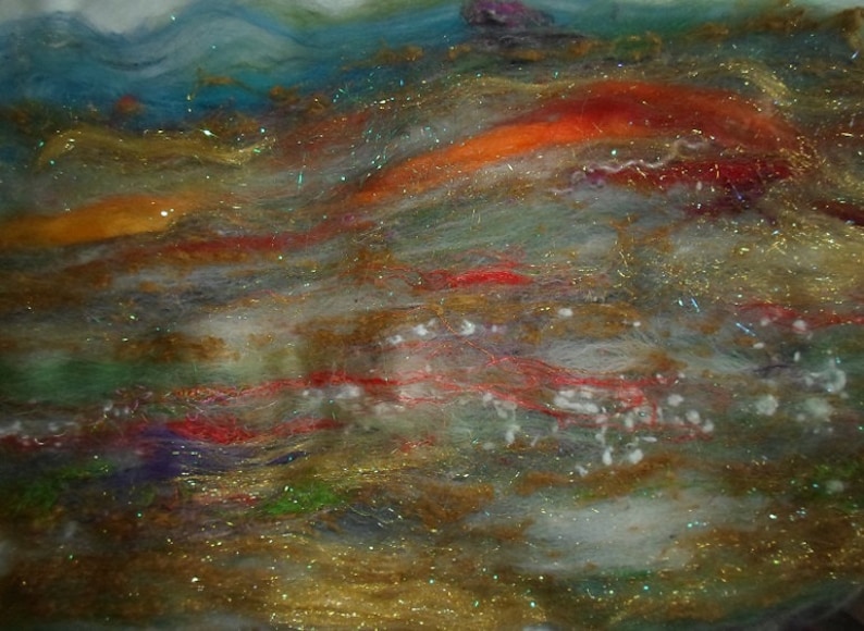 May include: Abstract art piece made with wool fibers in shades of blue, green, orange, red, and white. The fibers are layered and textured, creating a sense of depth and movement. The piece is accented with gold glitter, adding a touch of sparkle.