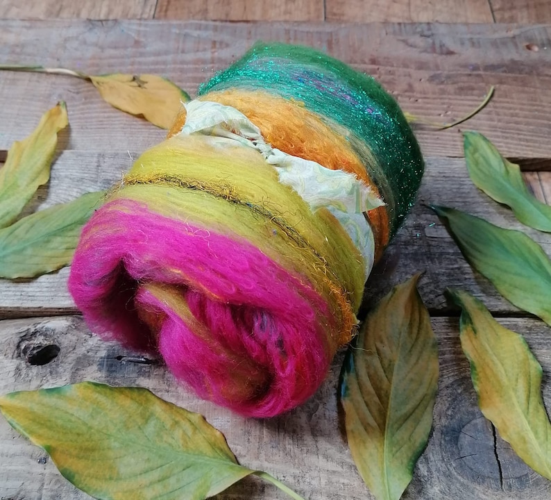 May include: A colorful ball of yarn with green, yellow, orange, and pink shades. The yarn is wrapped around itself and has a sparkly green layer on the outside.