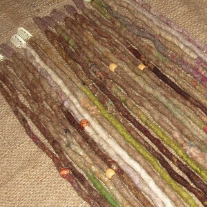 May include: A collection of brown, green, and white synthetic dreadlocks with wooden beads. The dreadlocks are arranged in rows and are ready to be added to hair.