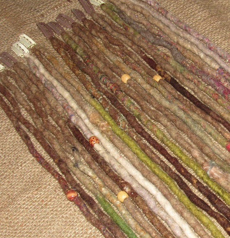 May include: A collection of brown, green, and white synthetic dreadlocks with wooden beads. The dreadlocks are arranged in rows and are ready to be added to hair.