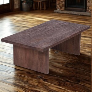 May include: A rectangular, dark brown wooden coffee table. The table has a simple, minimalist design with a flat top and two solid, rectangular legs. The wood grain is visible, adding texture to the piece. The table is approximately 48 inches long and 24 inches wide.
