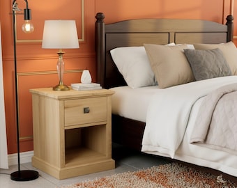 May include: A bedroom scene featuring a wooden nightstand with a drawer and open shelf, topped with a lamp. The bed has a dark brown headboard, white bedding, and decorative pillows. A black floor lamp stands to the left.