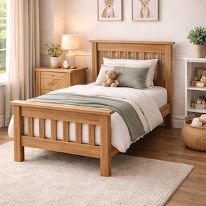 Peut inclure: Un lit en bois brun clair avec une tête de lit et un pied de lit. Le lit est fait avec une literie blanche, un plaid vert et un ours en peluche. La pièce comprend également une table de chevet, des œuvres d'art et un tapis. Le texte sur le mur indique "TÉLÉCHARGEMENT NUMÉRIQUE PLANS DE BOISSERIE."