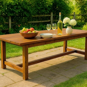 Puede incluir: Mesa de comedor exterior rectangular de madera con acabado natural. La mesa está puesta con una botella de vino, copas, platos, un jarrón con flores blancas y un cuenco de fruta. La mesa mide unos 200 cm de largo.