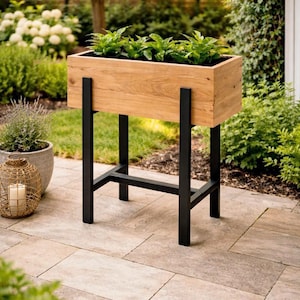 May include: A wooden planter box with green plants, supported by black metal legs. The planter is made of light-coloured wood and is placed outdoors on a patio. The design is modern and suitable for a garden or patio. The planter's dimensions are approximately 90cm in length.