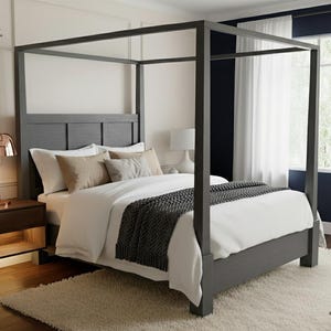 May include: A gray four-poster bed with a headboard, white bedding, and a dark gray throw blanket. The bed is in a bedroom with a nightstand, a lamp, and a fluffy rug. The room has white walls and a window with white curtains.