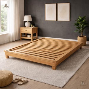 以下が含まれることがあります： スラットデザインの明るい色の木製ベッドフレーム。ベッドフレームは長方形で、地面から低い位置にあります。フレームは、ナイトスタンド、ランプ、アートワークのある部屋の明るい灰色のラグの上にあります。