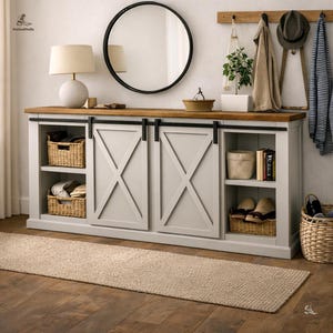 May include: A light gray cabinet with sliding doors and an X-shaped design. The cabinet has a wooden top and black hardware. Wicker baskets and other items are stored on the shelves. A round mirror and a lamp are visible.