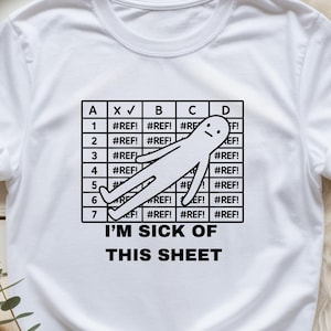 May include: White t-shirt with a black graphic. The graphic features a grid with the text "I'M SICK OF THIS SHEET" and a stick figure. The grid contains the text "#REF!" and check marks.