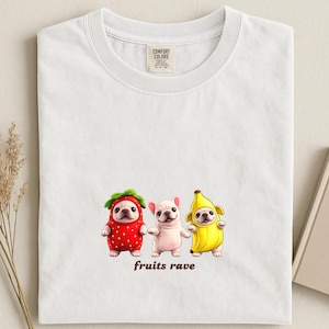 May include: White t-shirt with three cartoon French bulldogs dressed as a strawberry, a plain dog, and a banana. The phrase "fruits rave" is printed below the dogs. The shirt has a Comfort Colors tag.