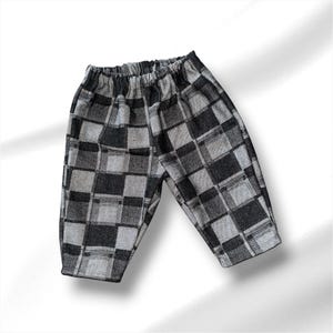 May include: A pair of trousers featuring a black and grey checkered plaid pattern. The garment has an elasticated waistband and a straight-leg cut, constructed from a woven fabric with a visible texture throughout the entire surface of the trousers.