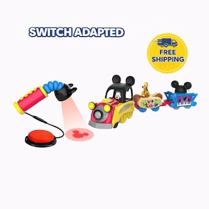 May include: A colorful toy train set featuring Mickey Mouse and friends. The train has a red, yellow, and black color scheme. The set includes a switch-adapted light and a red button. The text "SWITCH ADAPTED" is visible.