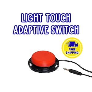 Może przedstawiać: Okrągły czerwony przełącznik adaptacyjny z czarną podstawą i czarnym przewodem zakończonym wtykiem jack 3,5 mm. Tekst LIGHT TOUCH ADAPTIVE SWITCH widnieje niebieskimi literami nad urządzeniem. Widoczna jest żółta okrągła odznaka z ikoną ciężarówki.