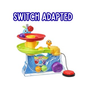 Può includere: Un giocattolo Playskool Switch Adapted con una base blu, una rampa a spirale verde e una funzione di caduta della palla rossa, gialla e viola. Il giocattolo ha un pulsante rosso e il testo "SWITCH ADAPTED" in blu.