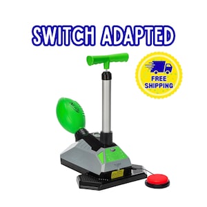 Könnte beinhalten: Ein schalteradaptierter Nerf-Spielzeugwerfer mit grünem Football, silbernem Pumpgriff und schwarzer Basis. Das Gerät verfügt über einen roten externen Druckknopf, der mit einem schwarzen Kabel verbunden ist. Der Text SWITCH ADAPTED ist sichtbar.