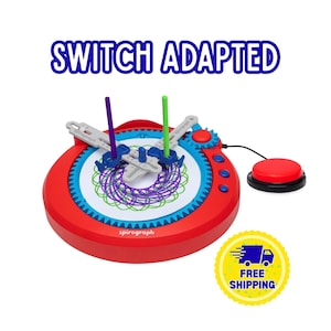 以下が含まれることがあります： SWITCH ADAPTEDという文字が書かれた赤と青のスピログラフ描画セット。円形のフレーム、紫と緑の幾何学模様が描かれた白い紙の中心部、2本の直立したペン、そして接続された赤い外部押しボタンが特徴です。