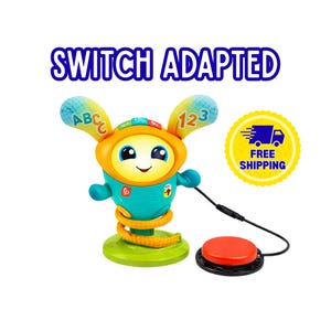 Pode incluir: Um brinquedo interativo adaptado com interruptor, apresentando um robô azul-petróleo e laranja com orelhas grandes marcadas com ABC e 123, um rosto sorridente e uma base de mola. Um cabo preto conecta o robô a um botão vermelho circular.