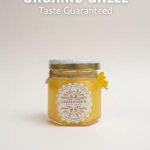 Könnte beinhalten: Ein Glas Bio-Ghee mit dem Etikett "GHEELICIOUS PURE GHEE". Das Glas ist mit einem goldenen Deckel verschlossen und mit Bindfaden und einer gelben Blume gebunden. Der Text oben lautet "ORGANIC GHEEE Taste Guaranteed".