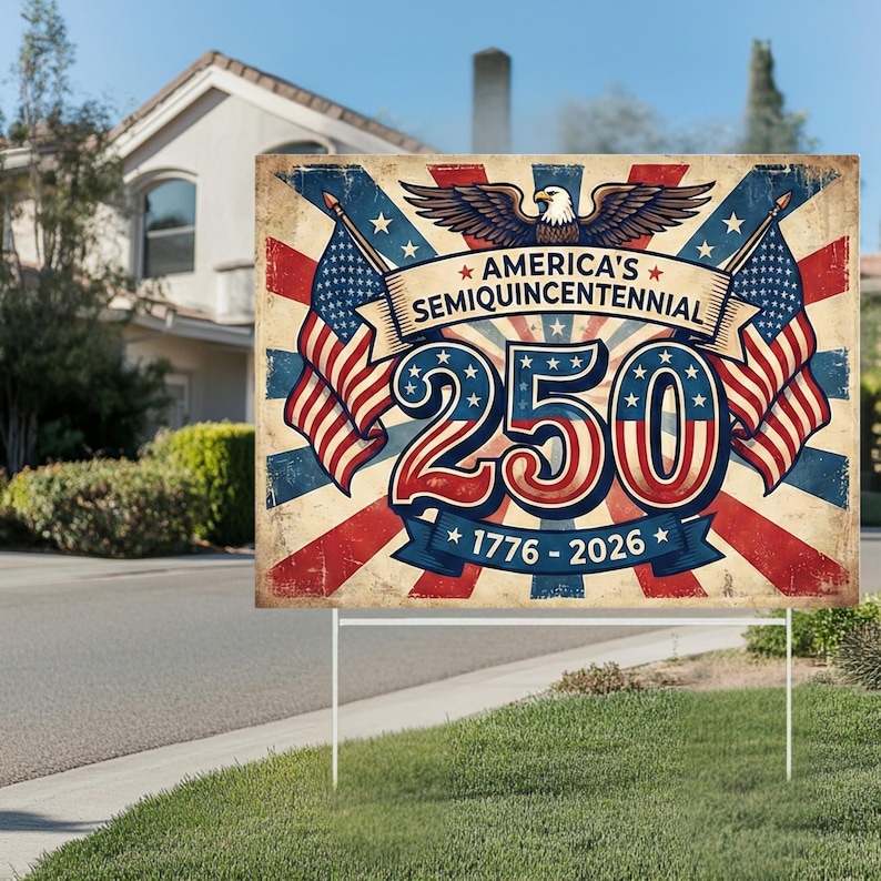 May include: A rectangular sign with the text "AMERICA'S SEMIQUINCENTENNIAL 250 1776-2026" in red, white, and blue. The sign features American flags and an eagle graphic. The sign is displayed on a lawn.