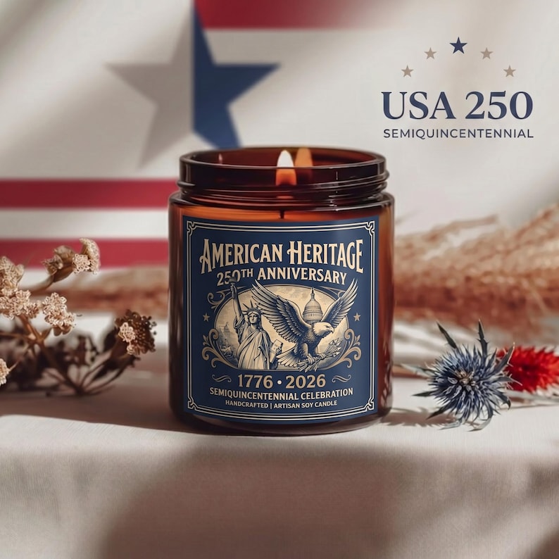 May include: A lit, amber-colored glass jar candle with a blue label that reads "American Heritage 250th Anniversary." The label features an eagle, the Statue of Liberty, and the years 1776-2026. The background includes a flag.