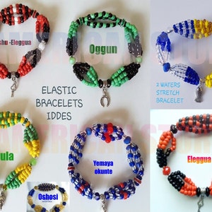May include: A collection of elastic bracelets in various colors, including red, black, green, yellow, and blue. Each bracelet is adorned with beads and charms, with text labels such as "Eshu-Eleggua" and "Oggun". The bracelets are designed as IDDES.