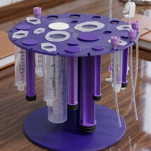 May include: A purple circular medical syringe organizer stand with multiple slots holding various clear plastic syringes and medical tubing. The stand features a central pillar and a flat base, with several syringes labeled VESCO hanging vertically.