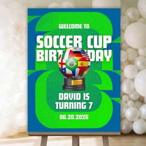 以下が含まれることがあります： イーゼルに飾られたサッカーをテーマにした誕生日パーティーのサイン。サインは緑と青で、「Welcome to Soccer Cup Birthday」と書かれています。旗で飾られたサッカーボールと「David is turning 7」の文字が特徴です。