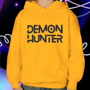 May include: Mustard yellow hoodie with the text "DEMON HUNTER" in black block letters. The hoodie has a front pocket and a hood. The background is a dark gradient with white and blue neon lines.