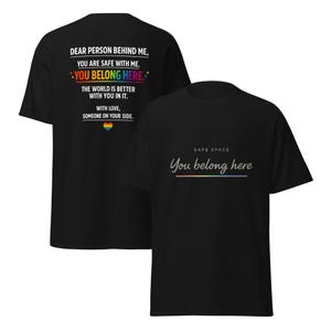 May include: Black t-shirts with text. One shirt has the text "DEAR PERSON BEHIND ME, YOU ARE SAFE WITH ME. YOU BELONG HERE. THE WORLD IS BETTER WITH YOU IN IT. WITH LOVE, SOMEONE ON YOUR SIDE." The other shirt says "SAFE SPACE You belong here."