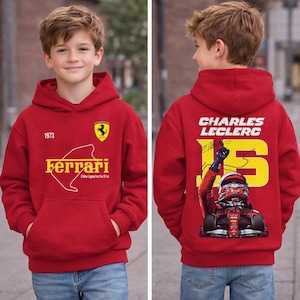 Może przedstawiać: Czerwona bluza z kapturem Ferrari z przednią grafiką przedstawiającą logo Ferrari, rok 1973 i napis "Ferrari". Tył bluzy z kapturem przedstawia "CHARLES LECLERC" i numer 16, wraz z wizerunkiem samochodu wyścigowego.