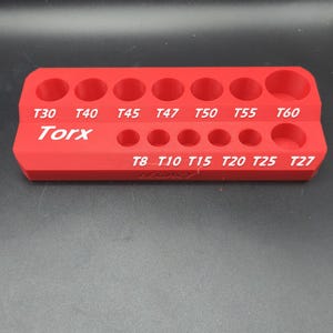 May include: A red rectangular Torx bit organizer tray featuring two rows of circular holes for storage. The top row is labeled T30, T40, T45, T47, T50, T55, and T60. The bottom row is labeled T8, T10, T15, T20, T25, and T27 in white text.