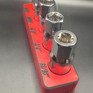 May include: A white ceramic mug with a black handle and the text "But First, Coffee" in a bold, black font. The mug is set against a blurred background, suggesting a cozy setting.