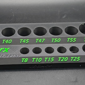 May include: A gray and black Torx bit holder with green lettering. The holder has multiple circular openings for various bit sizes, labeled T8 to T60. The text "Torx" and "21ZEFTXY" are also visible.
